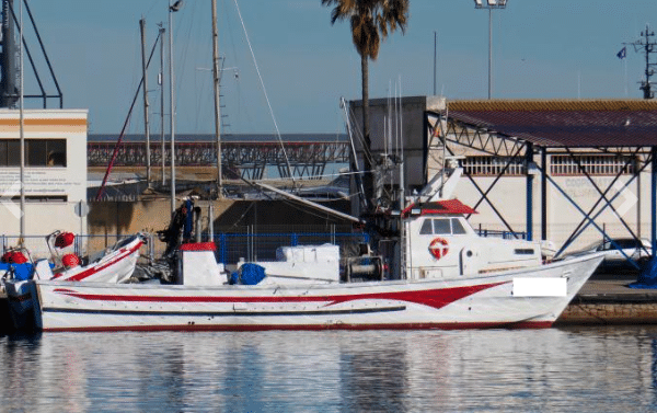 Barco de arrastre tradicional amarrado en puerto, pintado de blanco y rojo, reflejando las embarcaciones disponibles para la compra de segunda mano